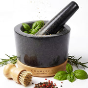 Granite mortar and pestle on a bamboo base with basil, peppercorns and a cleaning brush